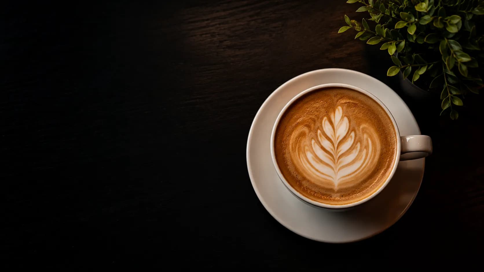 Capuchino con arte latte visto desde arriba sobre una mesa oscura.